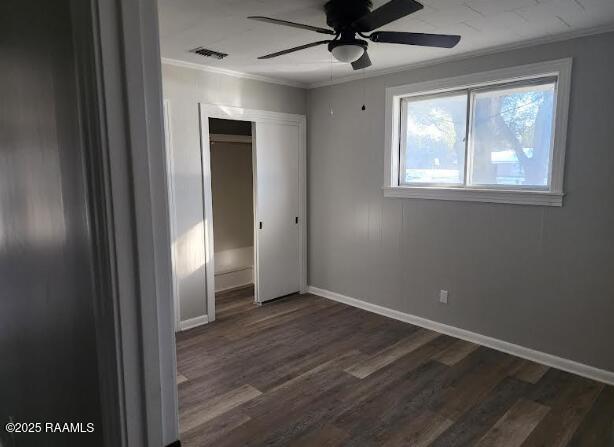 unfurnished bedroom featuring crown molding, dark wood-type flooring, a closet, and ceiling fan