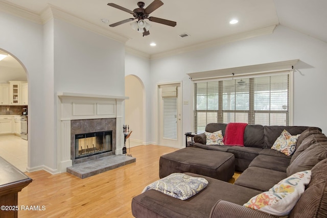 living room featuring ceiling fan, crown molding, a tiled fireplace, and light wood-type flooring