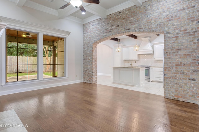 unfurnished living room with beam ceiling, ceiling fan, sink, and light hardwood / wood-style flooring