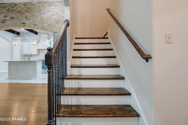 stairs featuring brick wall, wood-type flooring, and sink