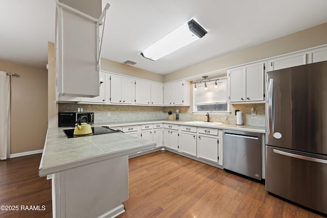 kitchen with wood-type flooring, white cabinetry, stainless steel appliances, sink, and kitchen peninsula