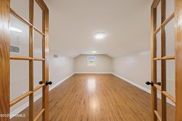 bonus room featuring light wood-type flooring, french doors, and vaulted ceiling