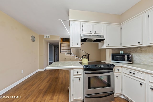 kitchen with white cabinets, appliances with stainless steel finishes, tasteful backsplash, kitchen peninsula, and hardwood / wood-style flooring