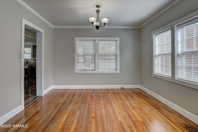 empty room featuring hardwood / wood-style flooring, ornamental molding, plenty of natural light, and an inviting chandelier