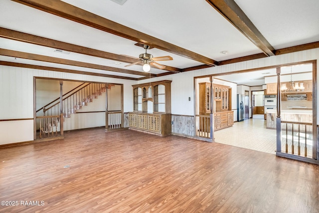 unfurnished living room with visible vents, beam ceiling, light wood-style flooring, a ceiling fan, and stairway