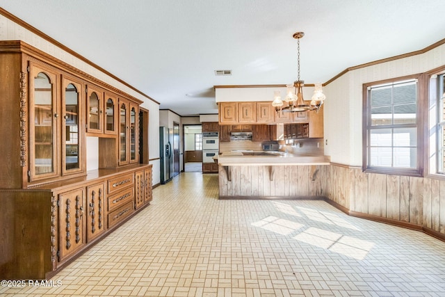 kitchen with a notable chandelier, a peninsula, wooden walls, and stainless steel fridge with ice dispenser