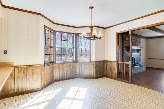 unfurnished dining area featuring a wainscoted wall, wallpapered walls, a wood stove, and ornamental molding