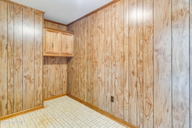 spare room with wooden walls, a textured ceiling, crown molding, and baseboards