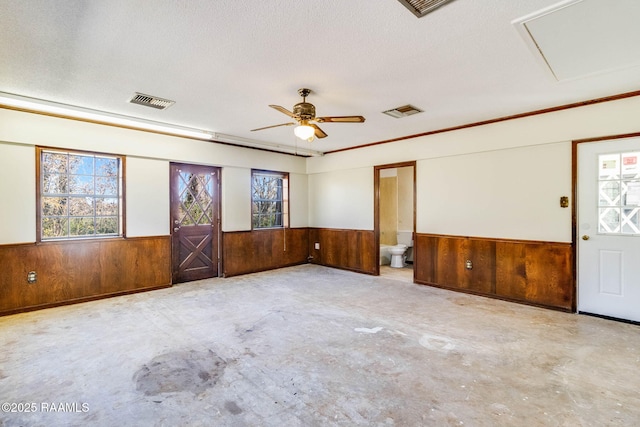 empty room with a textured ceiling, wood walls, and wainscoting