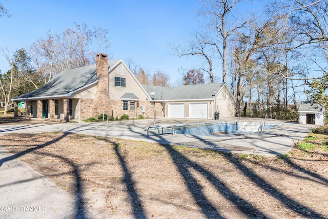 rear view of property featuring brick siding, driveway, a chimney, and an attached garage