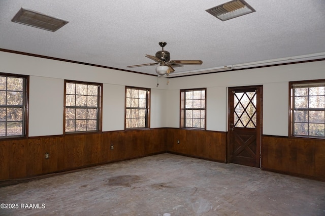 unfurnished room featuring visible vents, unfinished concrete flooring, a textured ceiling, wooden walls, and wainscoting