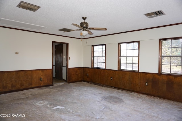 empty room with visible vents, a textured ceiling, concrete flooring, and wainscoting