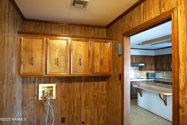 laundry area with visible vents, a textured ceiling, cabinet space, wood walls, and hookup for a washing machine