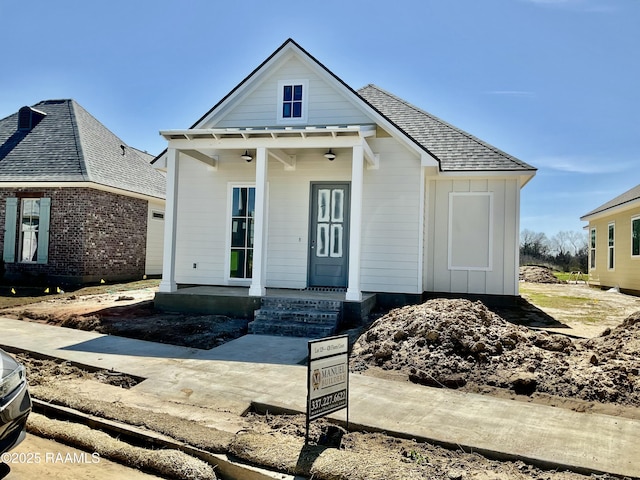 view of front facade featuring board and batten siding, covered porch, and roof with shingles