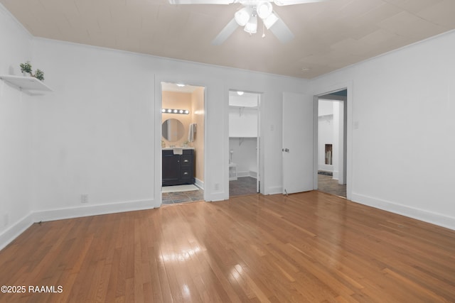 unfurnished bedroom featuring hardwood / wood-style flooring, ornamental molding, a walk in closet, ceiling fan, and a closet