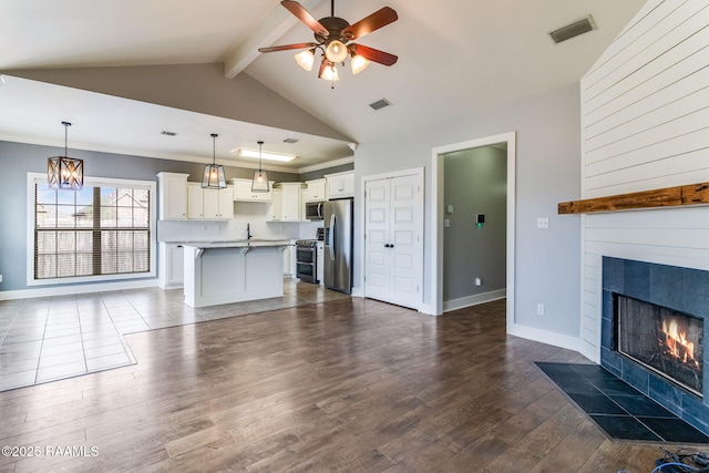 unfurnished living room featuring beamed ceiling, dark hardwood / wood-style flooring, a tiled fireplace, and ceiling fan with notable chandelier