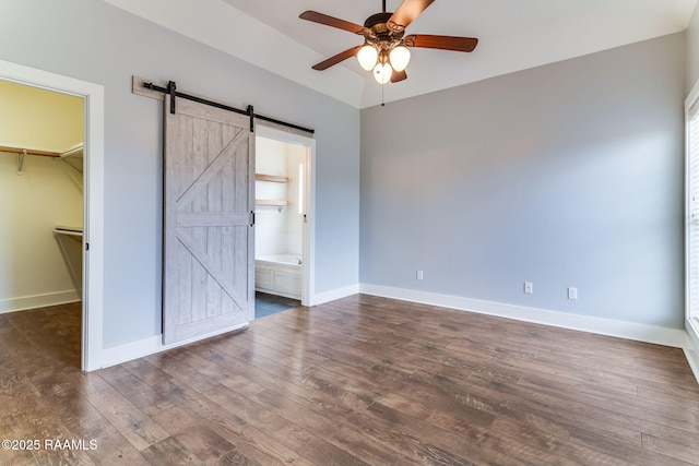 unfurnished bedroom featuring ceiling fan, connected bathroom, a barn door, a walk in closet, and a closet