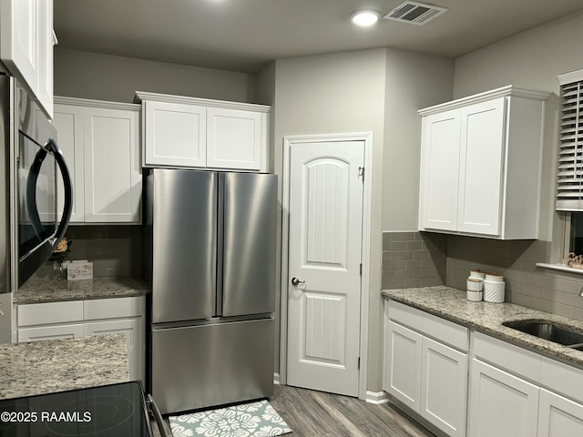 kitchen featuring white cabinetry, stainless steel fridge, and light stone counters