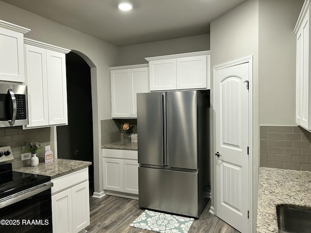 kitchen with white cabinetry, light stone counters, dark wood-type flooring, and appliances with stainless steel finishes