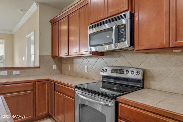 kitchen with tasteful backsplash, ornamental molding, tile countertops, and stainless steel appliances