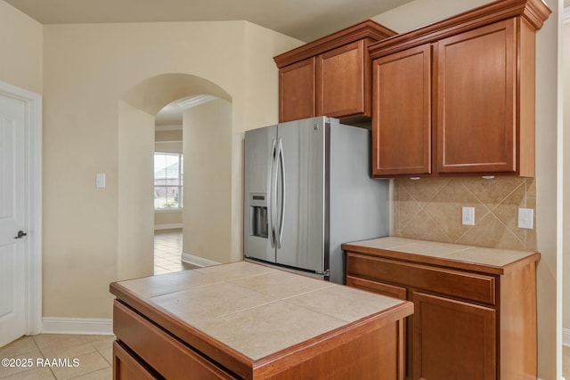 kitchen featuring tile counters, light tile patterned floors, backsplash, and stainless steel fridge