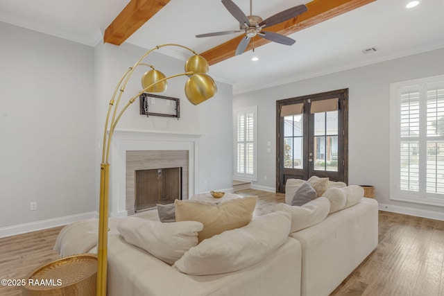 living room with a healthy amount of sunlight, light hardwood / wood-style flooring, ornamental molding, and beamed ceiling