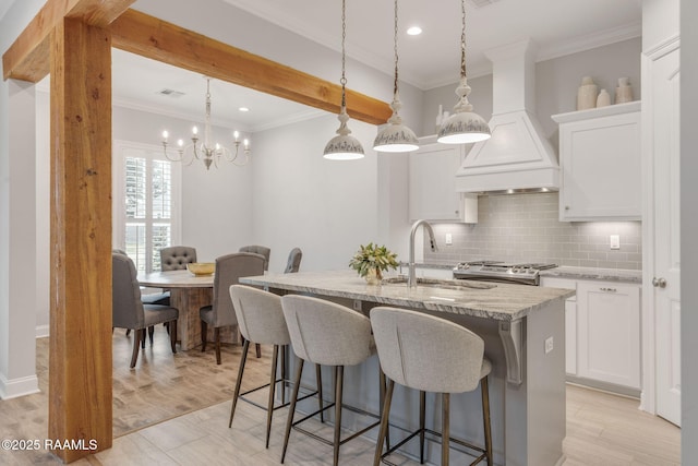 kitchen with a kitchen island with sink, hanging light fixtures, light stone countertops, white cabinets, and custom exhaust hood