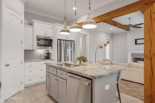 kitchen with beamed ceiling, sink, white cabinets, stainless steel appliances, and a center island with sink