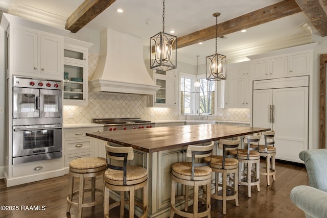 kitchen with a kitchen island, custom exhaust hood, butcher block counters, stainless steel appliances, and beam ceiling