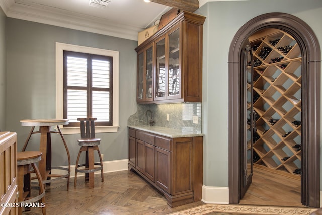 bar with dark parquet flooring, decorative backsplash, sink, light stone counters, and crown molding