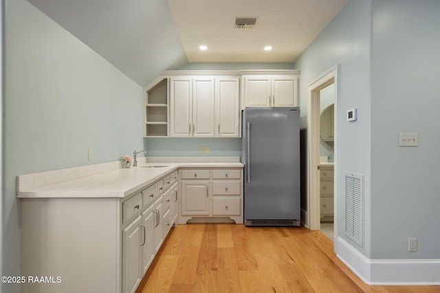 kitchen with sink, vaulted ceiling, white cabinetry, and stainless steel refrigerator