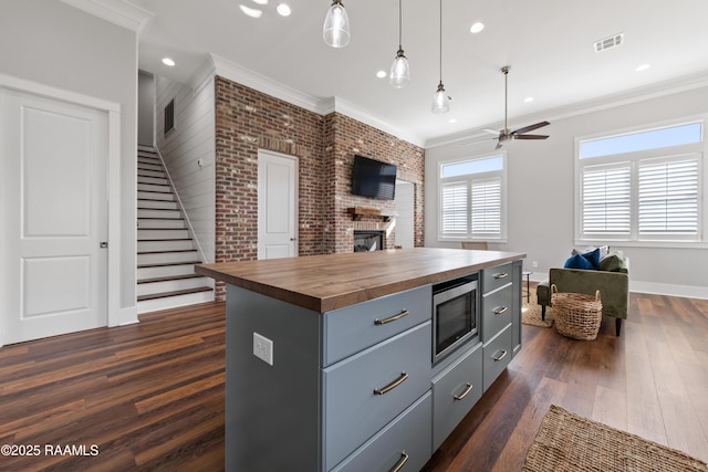 kitchen with crown molding, butcher block counters, hanging light fixtures, stainless steel microwave, and a kitchen island