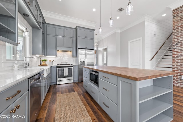 kitchen featuring butcher block counters, crown molding, decorative light fixtures, appliances with stainless steel finishes, and a kitchen island