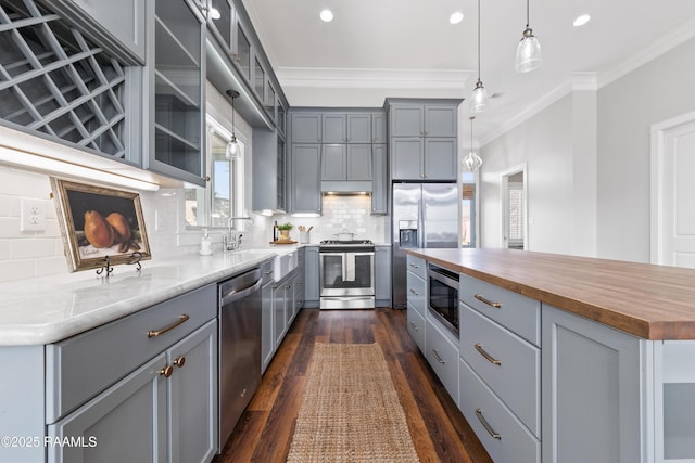 kitchen featuring backsplash, stainless steel appliances, ornamental molding, a kitchen island, and wood counters