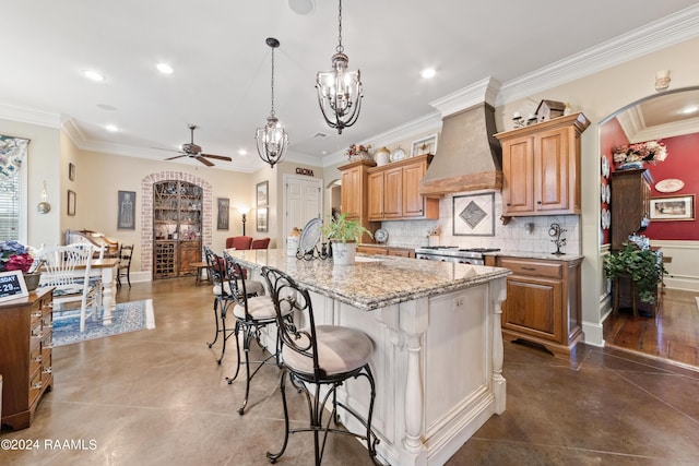 kitchen featuring premium range hood, a breakfast bar, light stone counters, hanging light fixtures, and a center island with sink