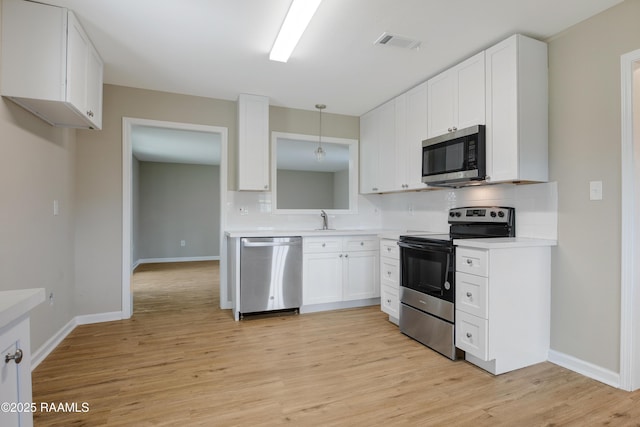 kitchen with white cabinetry, decorative light fixtures, light wood-type flooring, stainless steel appliances, and backsplash