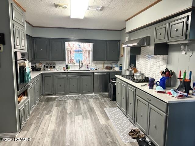 kitchen featuring gray cabinets, sink, backsplash, stainless steel appliances, and wall chimney range hood