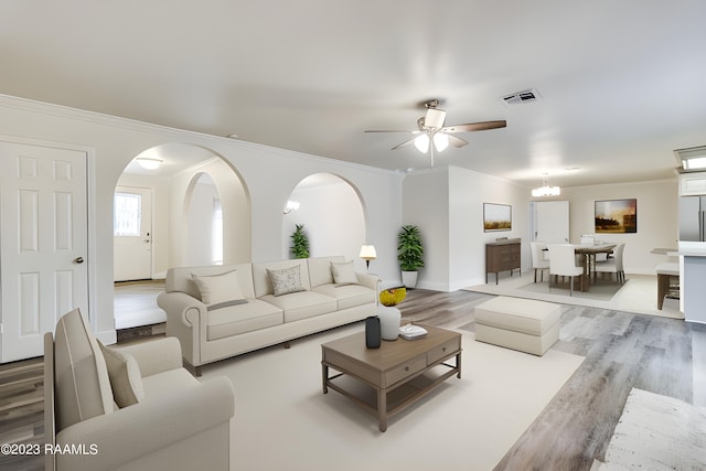 living room with crown molding, ceiling fan with notable chandelier, and light wood-type flooring