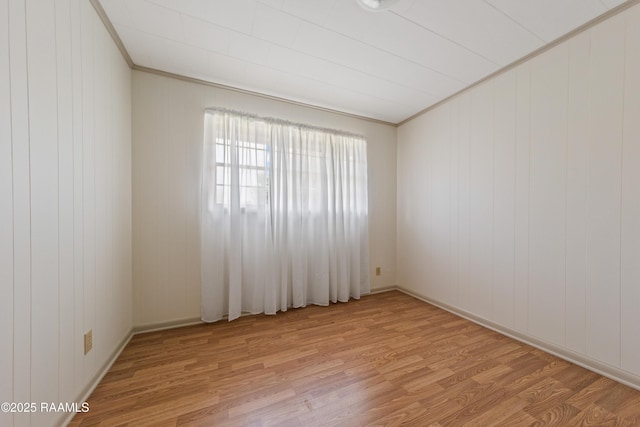 unfurnished room with light hardwood / wood-style flooring, ornamental molding, and wood walls