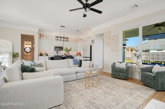 living room with crown molding, ceiling fan, and light wood-type flooring