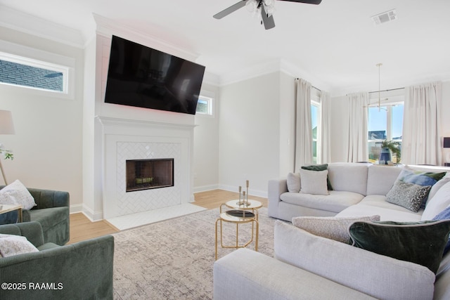 living room with a tiled fireplace, crown molding, plenty of natural light, and light wood-type flooring