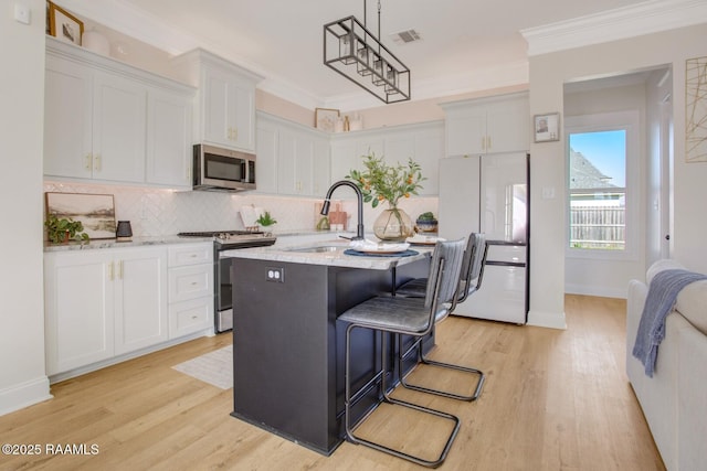 kitchen featuring sink, appliances with stainless steel finishes, a kitchen island with sink, white cabinets, and light wood-type flooring