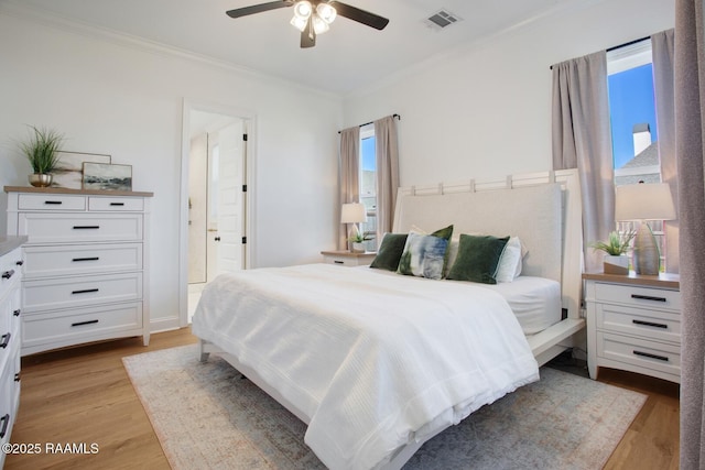 bedroom featuring ceiling fan, crown molding, light wood-type flooring, and ensuite bath