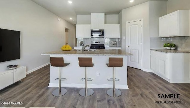 kitchen with tasteful backsplash, a kitchen breakfast bar, an island with sink, stainless steel appliances, and white cabinets