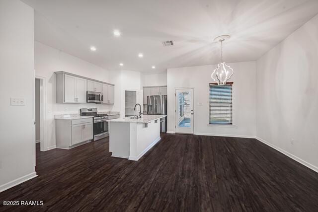 kitchen with decorative light fixtures, dark wood-type flooring, stainless steel appliances, and an island with sink