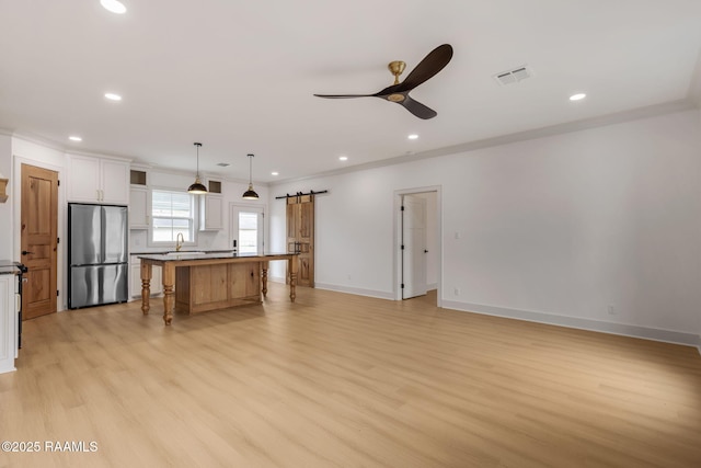 kitchen featuring pendant lighting, stainless steel refrigerator, white cabinets, a center island, and a barn door