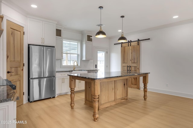 kitchen featuring a kitchen island, dark stone countertops, white cabinets, stainless steel fridge, and a barn door