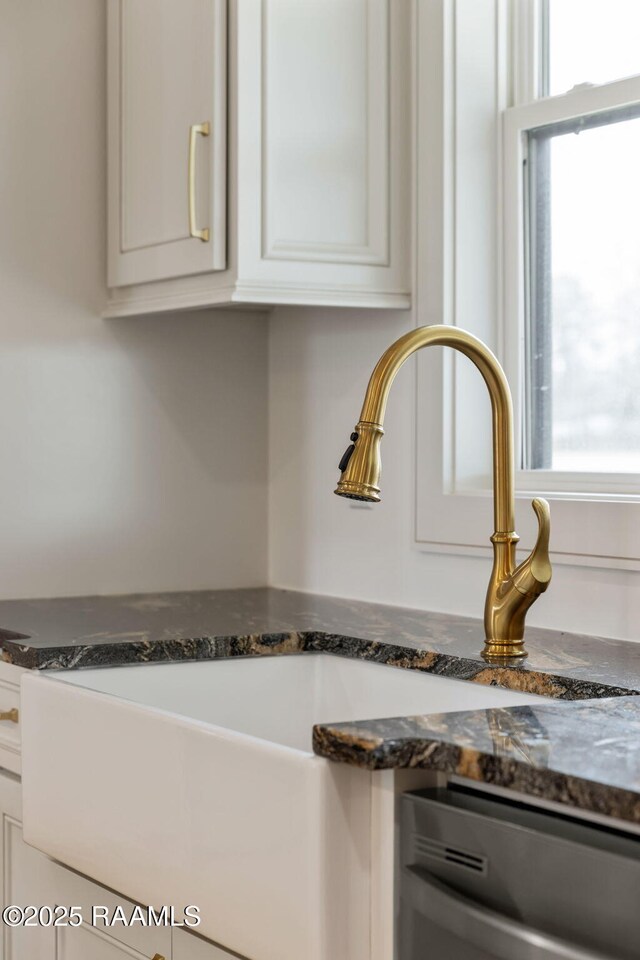 interior details featuring dark stone countertops, dishwasher, and white cabinets