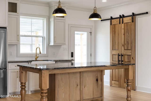 kitchen featuring decorative light fixtures, a center island, dark stone counters, a barn door, and white cabinets