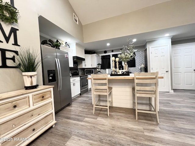 kitchen featuring white cabinetry, tasteful backsplash, light wood-type flooring, appliances with stainless steel finishes, and a kitchen breakfast bar